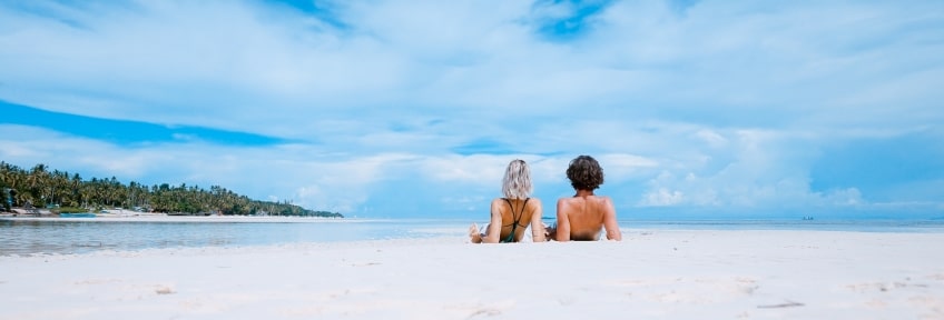 A man and a woman laying on the white sand shore