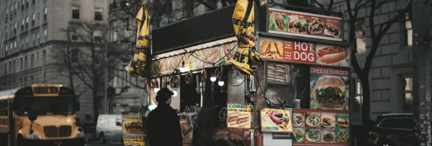 A man standing in front of a hot-dog cart